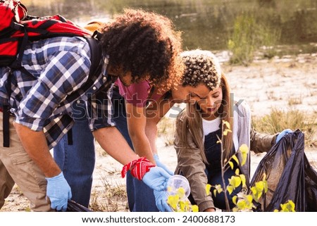 This image captures a moment of environmental stewardship, as a diverse group of volunteers engage in a community clean-up effort by a lake. The photograph features a Middle-Eastern man and a woman of Royalty-Free Stock Photo #2400688173
