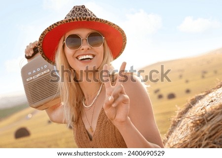 Happy hippie woman with radio receiver showing peace sign in field