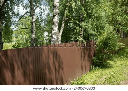 Solid fence in park. Private area in forest. Fenced area. Brown fence made of steel profile.