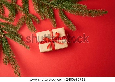 The gift is wrapped in craft paper and wrapped with a red ribbon on a red background. The concept of the New Year holidays.