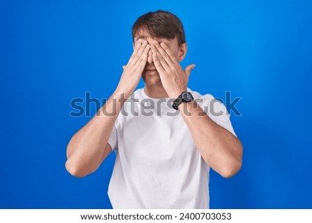 Caucasian blond man standing over blue background rubbing eyes for fatigue and headache, sleepy and tired expression. vision problem 