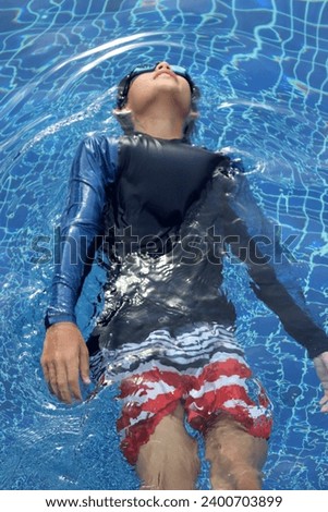 Photo top view of a little boy teen male who swims or floats in a swimming pool with blue tiles in a resort hotel during his summer vacations break 