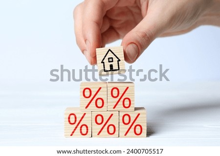 Mortgage rate. Woman building pyramid of cubes with house icon and percent signs at white wooden table, closeup