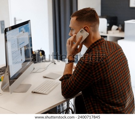 Young businessman working in the office. A programmer works at a computer. System administrator in the office. A man is talking on the phone and working at the computer.