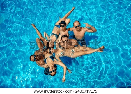 Group of happy young friends are having fun and posing for photo in swimming pool together