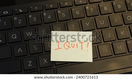 Side view of yellow adhesive note with handwritten capital-letter words "I quit" in red ink, placed on keyboard