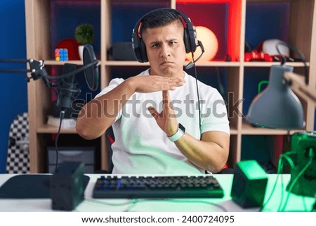 Young hispanic man playing video games doing time out gesture with hands, frustrated and serious face  Royalty-Free Stock Photo #2400724095