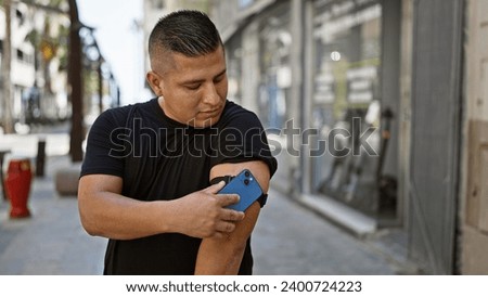 Confident young latin man, happily scanning his diabetes sensor on the city street using his smartphone, expertly monitoring his glucose levels, putting technology to work Royalty-Free Stock Photo #2400724223