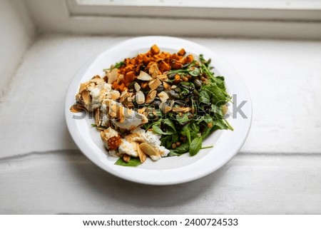 Healthy vegetarian or vegan food on a plate with sweet potato, almond, cheese, lentils and arugula on a white plate with white wooden background