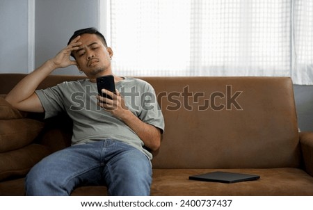 Asian young upset depressed man sitting alone in living room at home. Attractive unhappy male feeling very sad, lonely and frustrated with life problem think of money debt, bankruptcy.
 Royalty-Free Stock Photo #2400737437