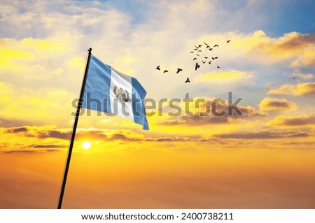 Waving flag of Guatemala against the background of a sunset or sunrise. Guatemala flag for Independence Day. The symbol of the state on wavy fabric.