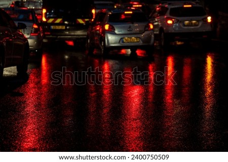 Abstract, wet asphalt road colorfully illuminated at night by red car taillights and traffic signal lights.