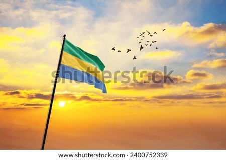 Waving flag of Gabon against the background of a sunset or sunrise. Gabon flag for Independence Day. The symbol of the state on wavy fabric. Royalty-Free Stock Photo #2400752339