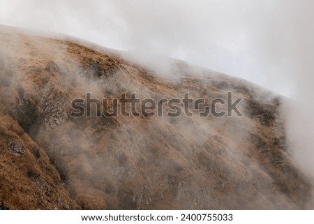 close up view of a grassy and rocky mountain side, partially covered by the clouds