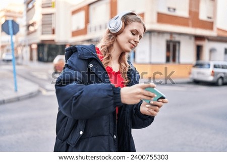 Young blonde woman smiling confident playing video game at street