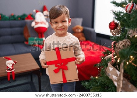 Adorable hispanic boy holding christmas gift standing at home
