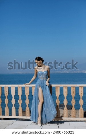Italian model posing in a blue sparkly dress with a view to the blue sea and volcano Vesuvius. 