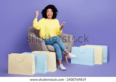 Full size photo of funny girl sit on armchair near bags hold smartphone celebrate black friday isolated on violet color background