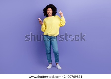 Full size photo of cheerful clever woman dressed yellow sweater hold smartphone showing v-sign isolated on violet color background