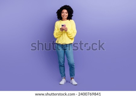 Full size photo of intelligent woman dressed yellow sweater denim pants texting message on smartphone isolated on violet color background