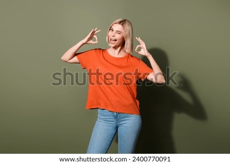 Photo portrait of attractive young woman winking okey symbol good job dressed stylish orange garment isolated on khaki color background