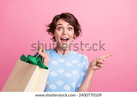 Photo of charming astonished girl hold store bags indicate finger empty space ad offer isolated on pink color background