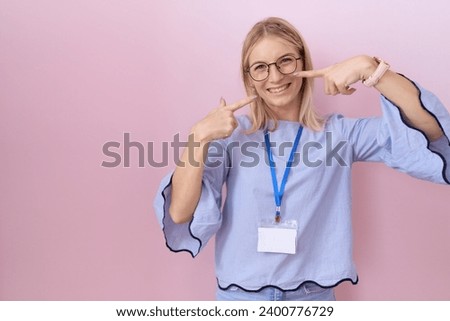 Young caucasian business woman wearing id card smiling cheerful showing and pointing with fingers teeth and mouth. dental health concept. 
