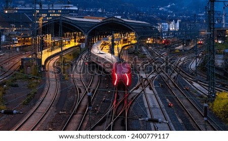 Main station wide angle panorama with tracks, platforms, signals and light traces of passing passenger trains in Hagen, Germany. Colorful early morning twilight atmosphere with longtime exposure. Royalty-Free Stock Photo #2400779117