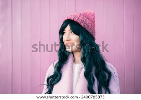 Stylish young smiling hipster woman with color hair wearing pink coat and knitted hat on pink wooden background. Urban seasonal city street fashion. Barbiecore style. Selective focus. Royalty-Free Stock Photo #2400785875