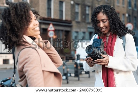 Professional female photographer is doing a photoshoot with a female model in the street. She is using an old medium format analog camera in a cold winter day. They are wearing thick winter coats.