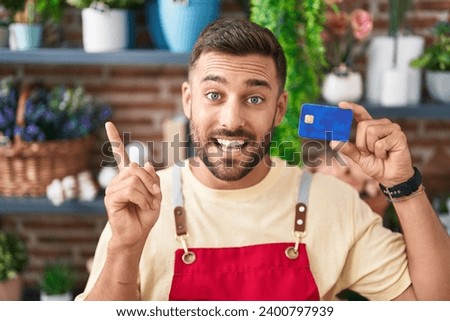 Handsome hispanic man working at florist shop holding credit card smiling happy pointing with hand and finger to the side  Royalty-Free Stock Photo #2400797939