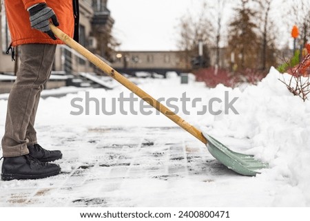 Close-up of a man cleaning and clearing snow in front of the house on a sunny and frosty day. Cleaning the street from snow on a winter day. Snowfall, and a severe snowstorm in winter. Royalty-Free Stock Photo #2400800471