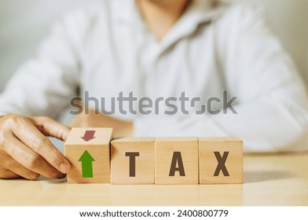 A man flip wooden cube with Down arrow change to UP arrow and TAX character. Concept of financial, stocks and interest rate