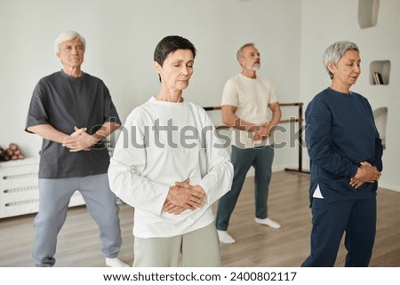 Wide shot of senior people doing breathing exercise during qigong class while pressing hands to stomach Royalty-Free Stock Photo #2400802117