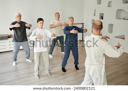 Wide shot of senior people meditating during qigong exercise in fitness studio while male instructor teaching Royalty-Free Stock Photo #2400802121