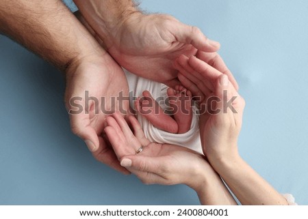 The palms of the parents, father and mother hold the legs, feet of a newborn baby in a white wrapper on a blue background. Feet, heels and toes of a newborn child close -up. Professional macro photo.