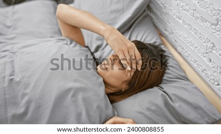 Exhausted young hispanic woman stressing out in her cozy bedroom, anxiously lying in bed with problematic expressions amidst morning haze Royalty-Free Stock Photo #2400808855