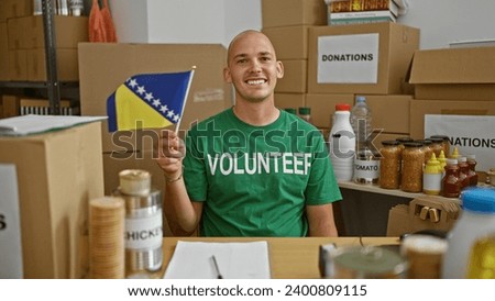 Young hispanic man volunteer smiling confident holding bosnian flag at charity center Royalty-Free Stock Photo #2400809115