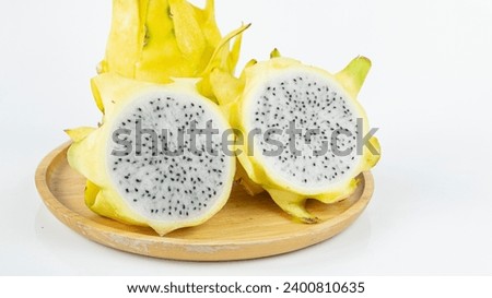 Close-up of an unusual bright yellow dragon fruit cut in half, white flesh, juicy, sweet, delicious, rich in vitamins, good for health in a wooden plate. on a white background