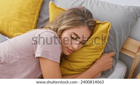 Young, beautiful blonde woman comfortably resting in cozy morning relaxation, lying asleep in bedroom bed, exhibiting ultimate relaxation within her warm indoor apartment room
