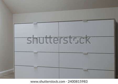 Capture the finesse of a white dresser up close within a chic, white-themed wardrobe room. Royalty-Free Stock Photo #2400815983