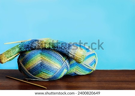 wool sock in the process of knitting, threads of variable colors of blue, green and yellow lie on a wooden table on a blue background