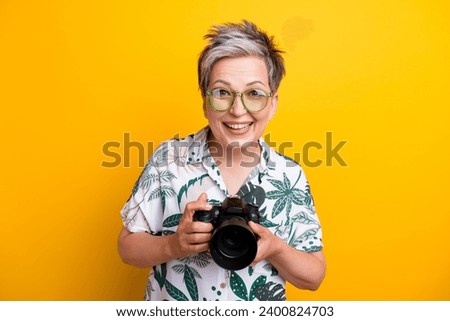 Photo portrait of lovely grandma excited hold professional camera wear trendy tropical print garment isolated on yellow color background