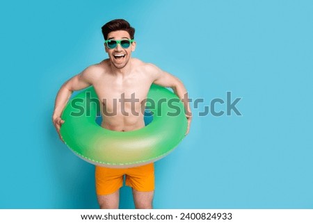Photo portrait of nice young male float ring have fun excited wear trendy yellow shorts isolated on blue color background summer vacation