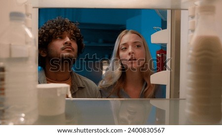 Point of view POV inside refrigerator Caucasian girl woman girlfriend wife and Arabian man Indian guy boyfriend husband multiracial couple at night evening open empty fridge at kitchen unhappy sad Royalty-Free Stock Photo #2400830567