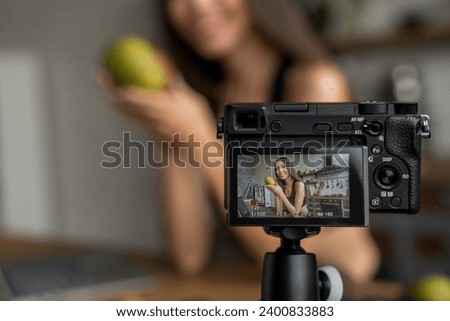 Young female blogger on camera screen holding mango for healthy eating vlog, defocused image. Weight loss, dieting, healthy living lifestyle