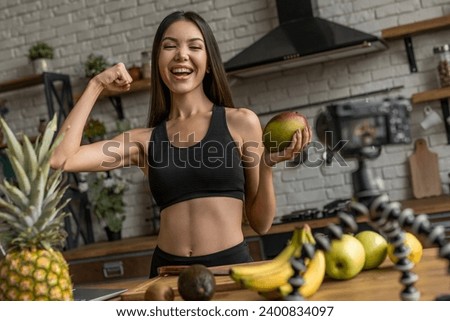Healthy blog! Young lady in sports wear recording video on tripod mounted camera in kitchen. Healthy eating habits, dietary supplements, weight loss, calories burning