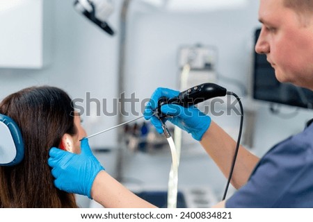 An ENT doctor performs an endoscopy procedure on a patient's ear in clinic holding a professional device in his hand Royalty-Free Stock Photo #2400834821
