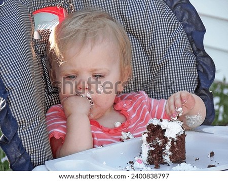 A little blond girl sitting in a high chair eating chocolate cake