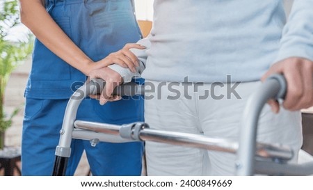 Cropped image of nurse helping senior woman to walk with walker at home. Walking movement disability impairment, handicapped person. Senior life concept Royalty-Free Stock Photo #2400849669